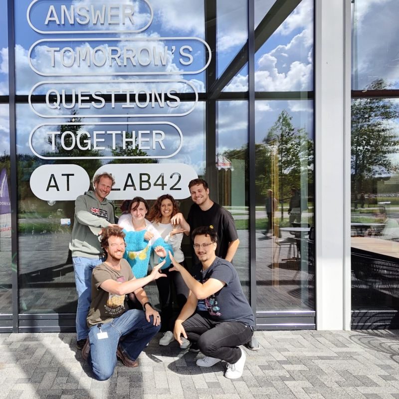 A group of seven people posing in front of the Lab42 building at the University of Amsterdam